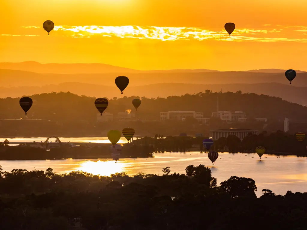 Hot air balloons are flying up during sunrise over the Lake Burley Griffin