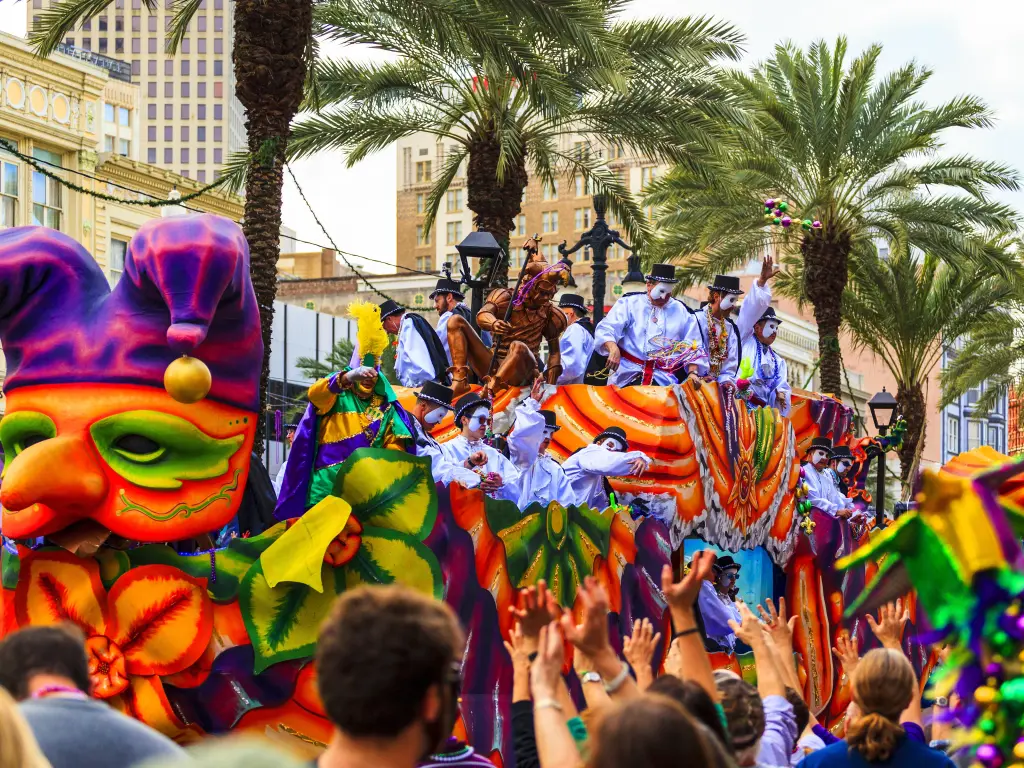 Colorful Mardi Gras parade with people in masks on the float, surrounded by spectators