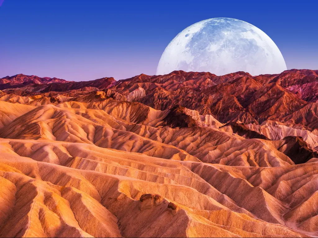 The moon rising over the rugged red rocks of Death Valley National Park