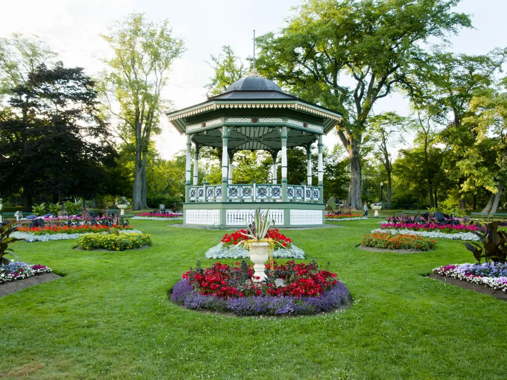 Beautiful white gazebo in the manicured garden with flower beds around it