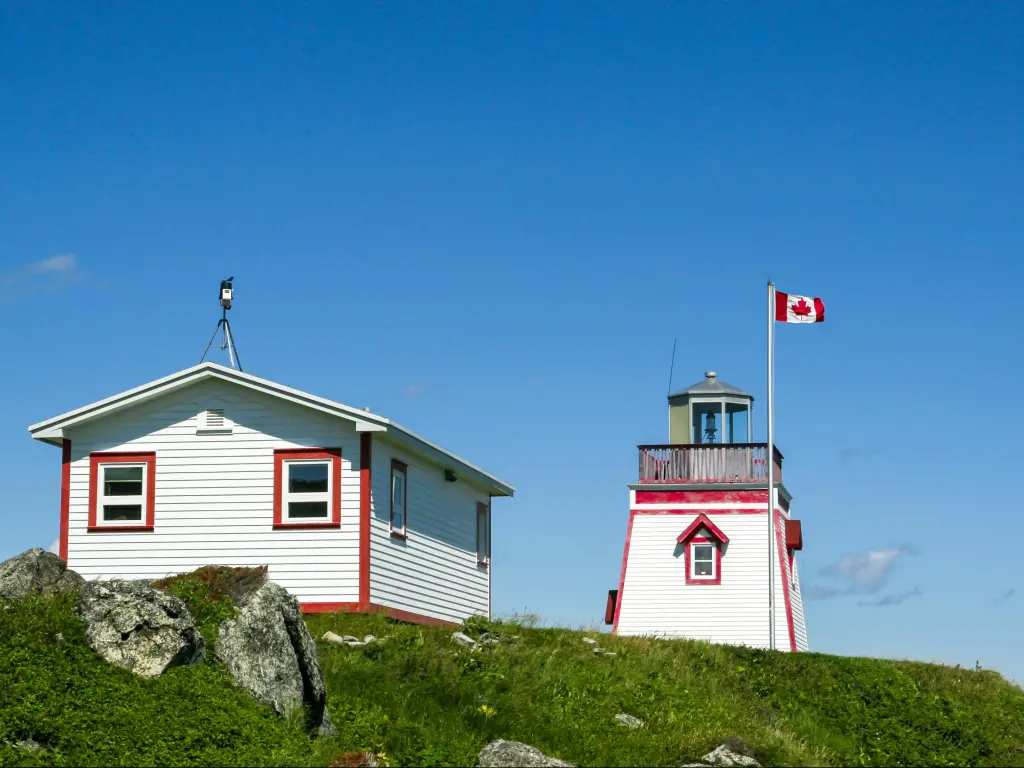 Wooden, boxy lighthouse building at St Anthony's, Newfoundland, with the Canadian flag flying set against the blue sky