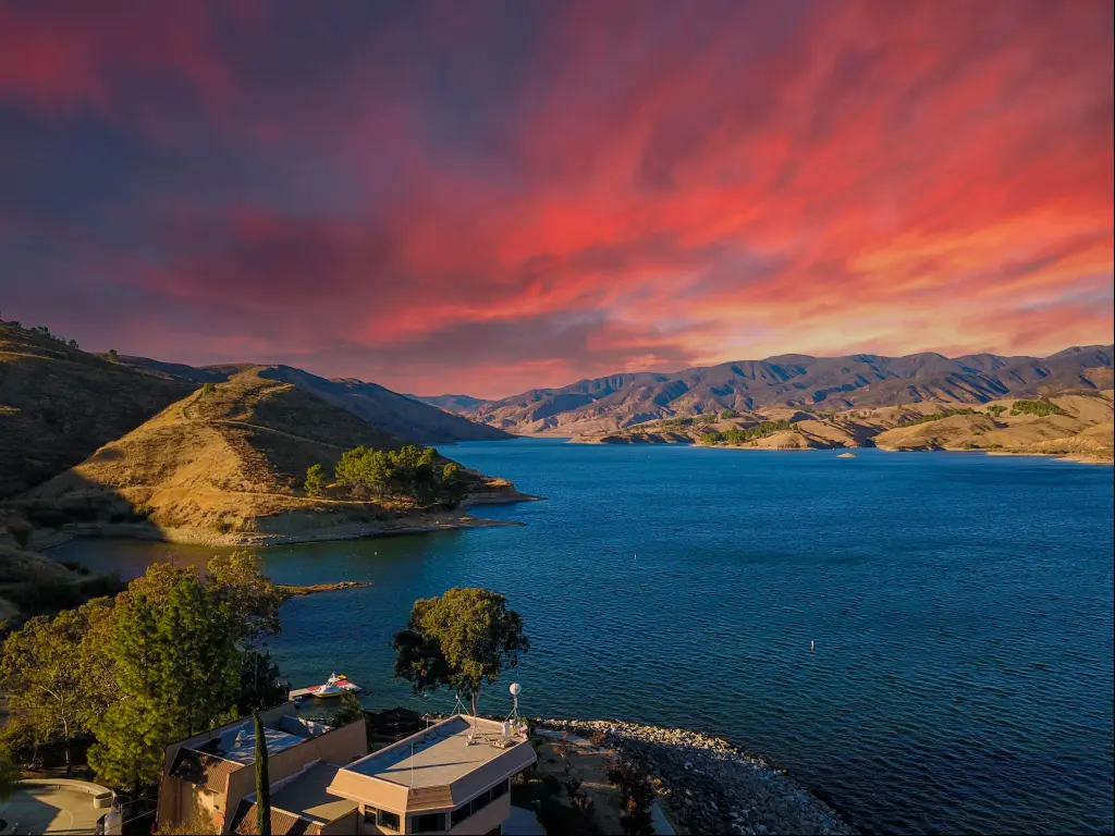 Aerial shot of the vast blue waters of Castaic Lake with majestic mountain ranges at sunset with a red sky in California