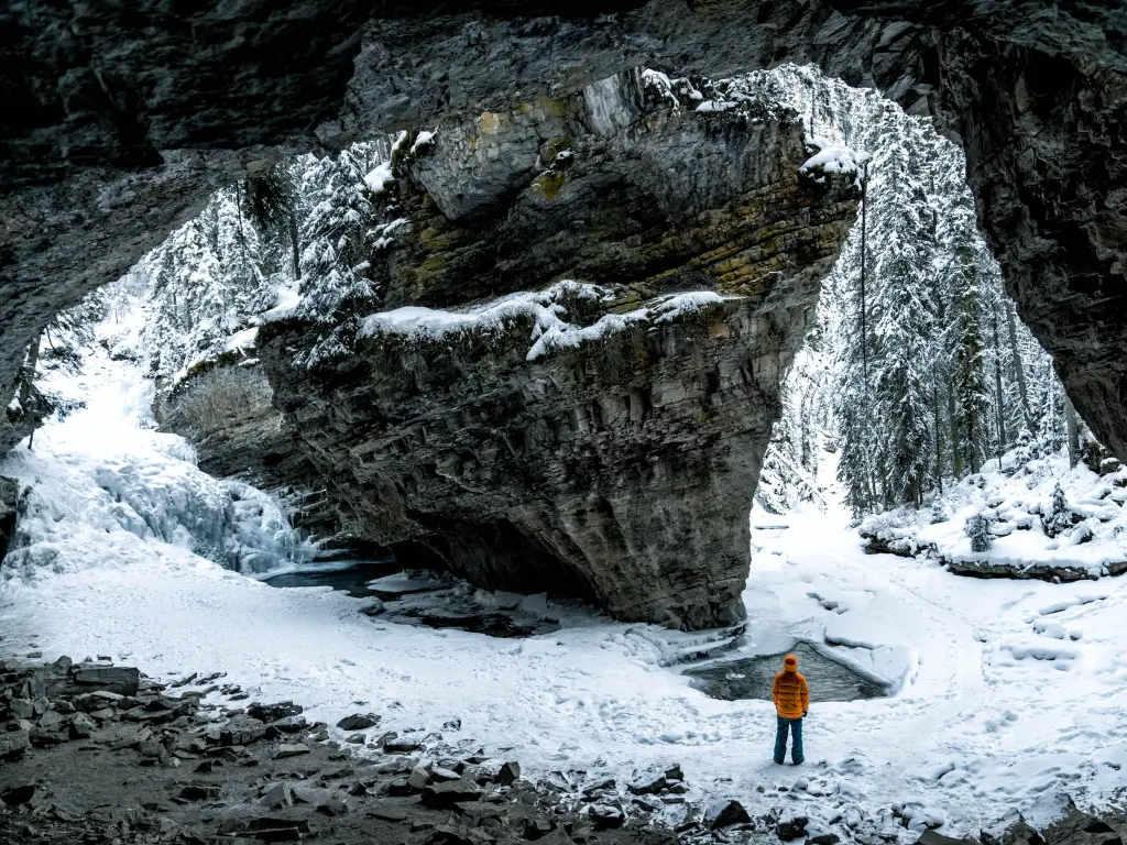 Canyon under snow, with a hiker wearing an orange jacket standing under rock formation