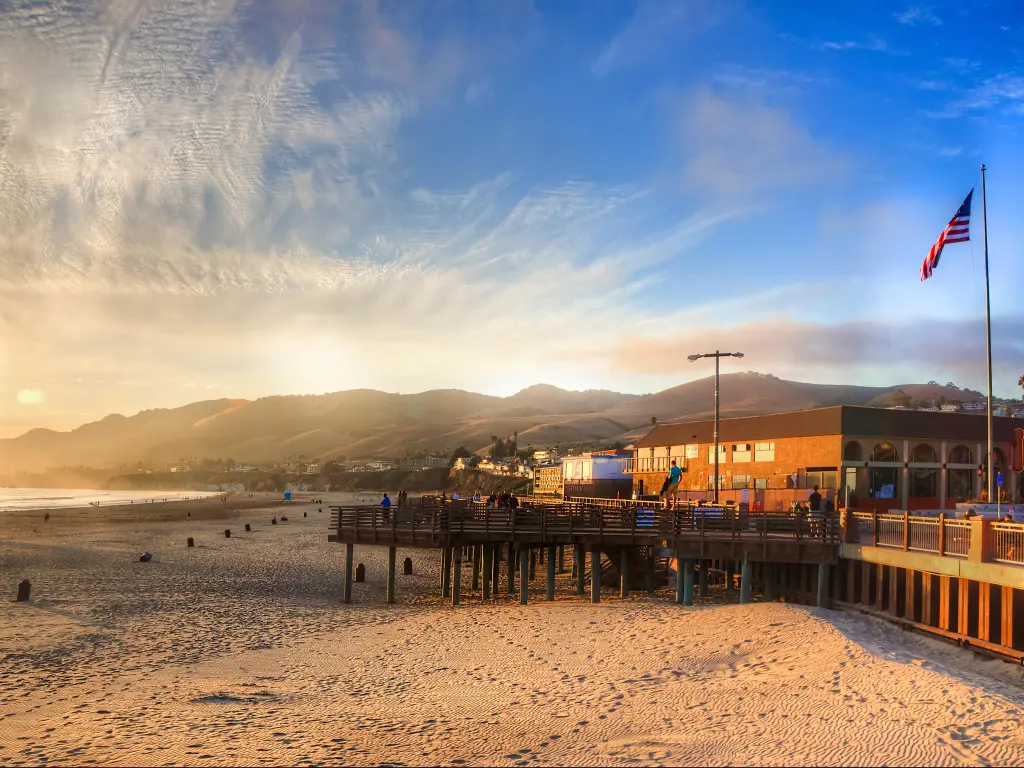A US flag flies on the wooden pier at Pismo Beach in California, with mist rising from the ocean