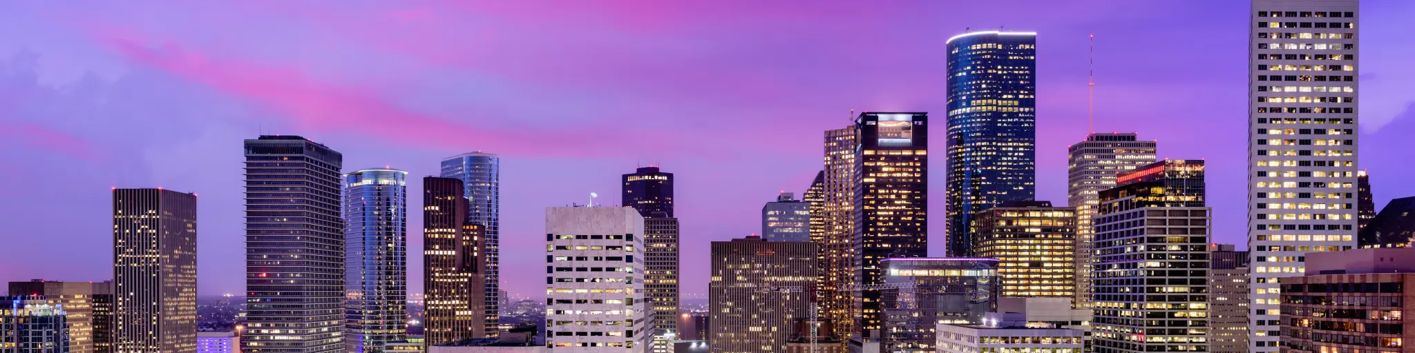 Skyline of the city during a pink and purple sunset with the buildings lit up 