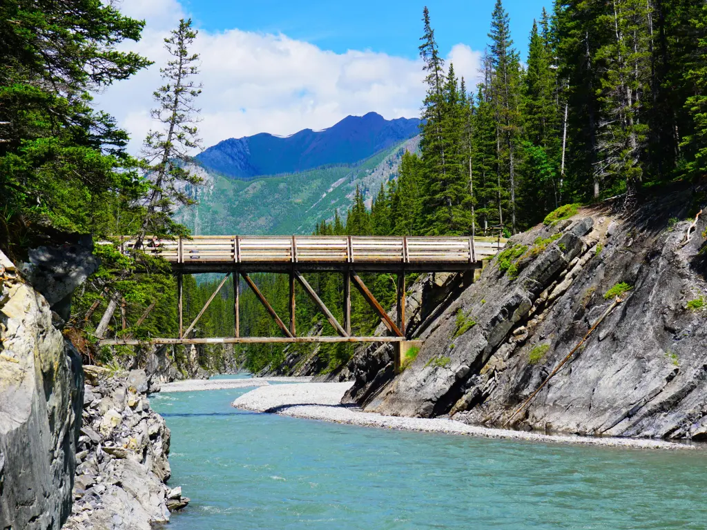 Canyon with a river running through it, wooden bridge running across on a bright day