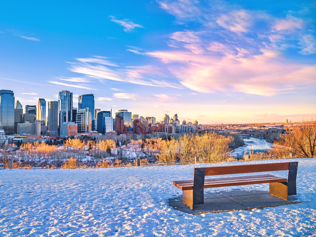 A view of the Calgary skyline on a blue-sky winter's day at sunrise, with a bench in the foreground