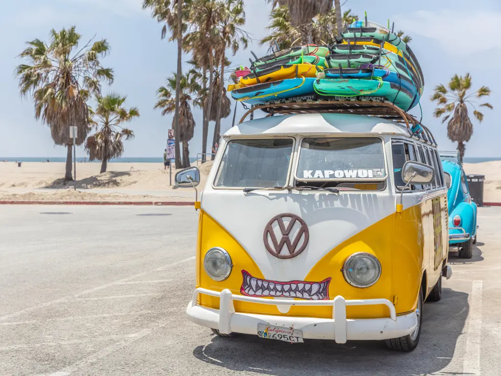 Yellow VW camper van with a cute mount drawn on it, parked with colorful paddleboards on top
