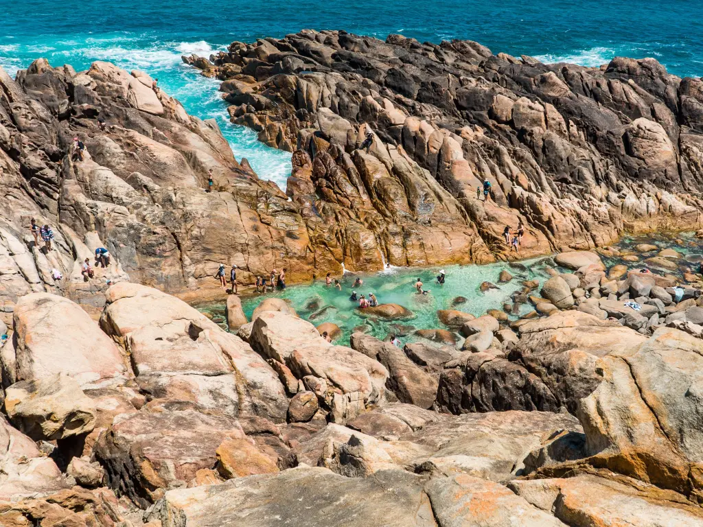 People enjoying a pool by the ocean, nestled in a rugged rock surrounding