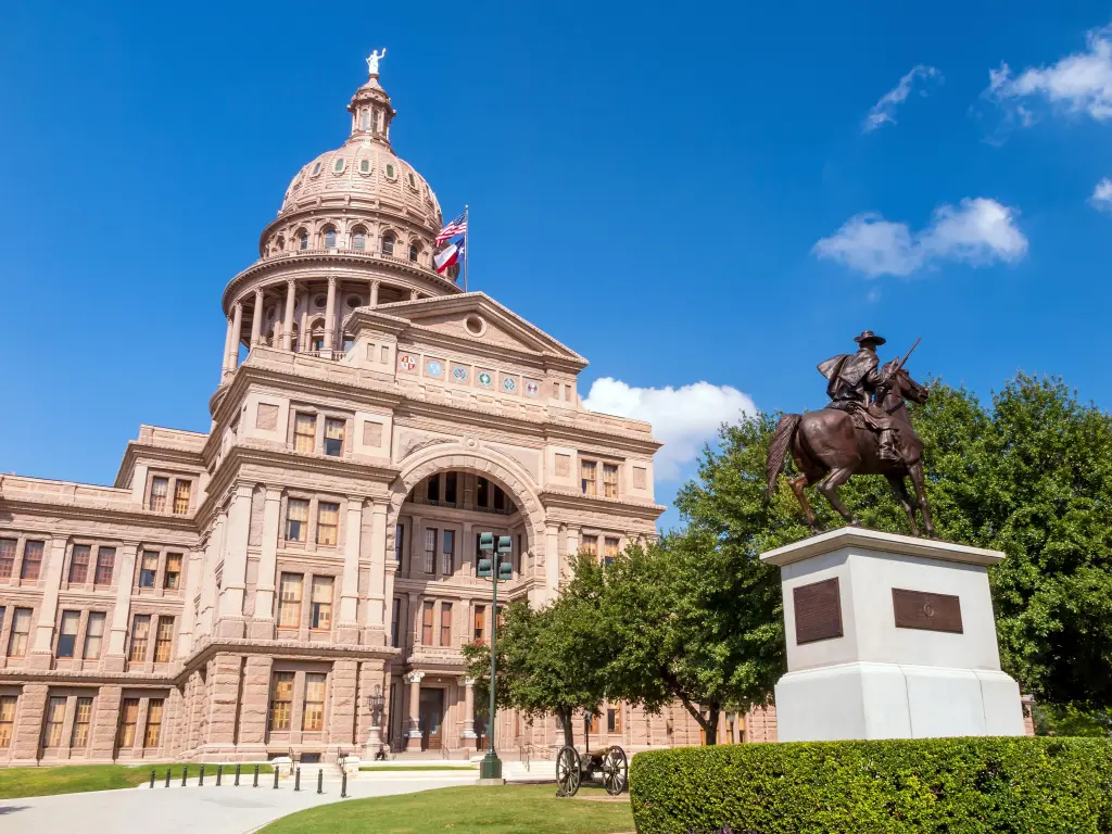 Exterior of the impressive capitol building with a statue in the front, on a sunny day