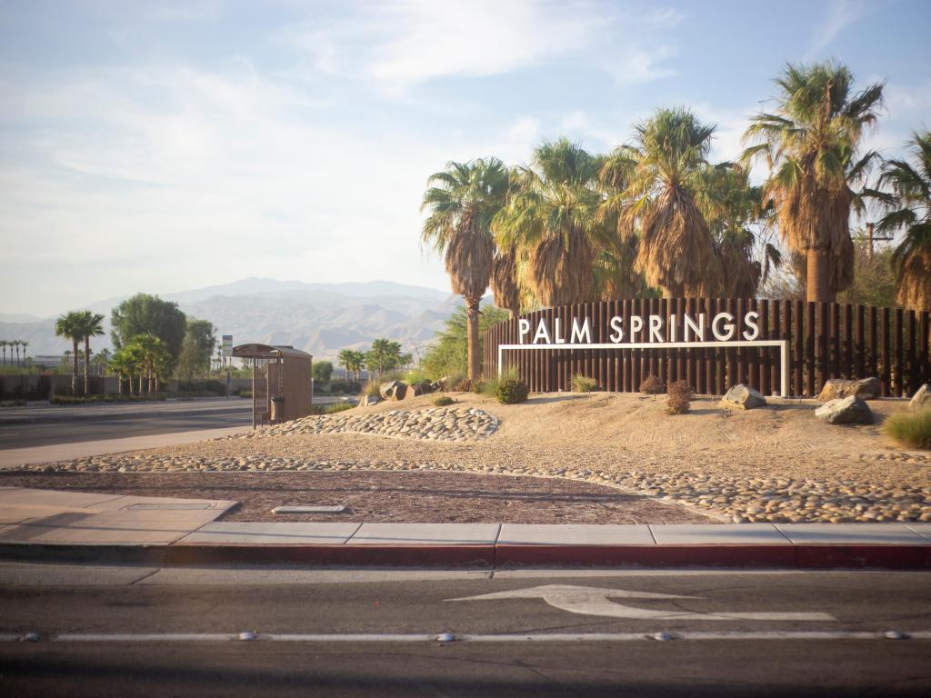 City of Palm Springs, California, USA with the sign and palm trees in the foreground and mountains in the distance.